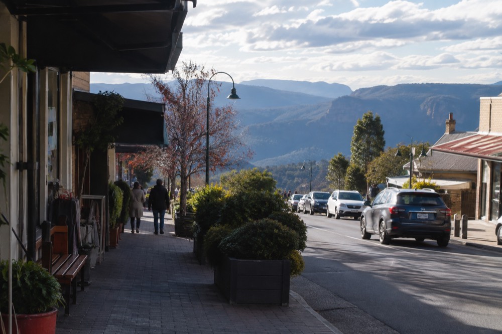 A village street lined with shops backed by blue-hazed mountain ridges