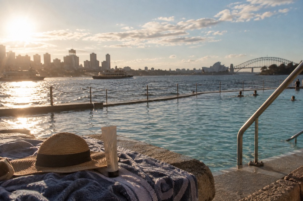 Sunscreen and a hat on a towel beside an ocean pool overlooking Sydney's coastline