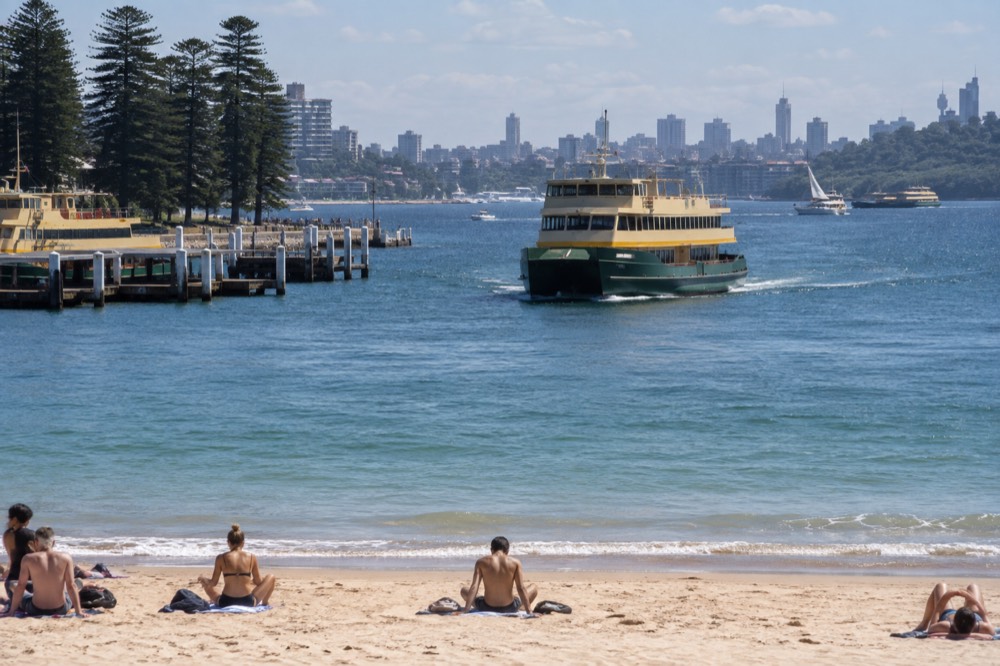 A green and yellow Sydney ferry approaching Manly Wharf with calm water and ferries moored nearby