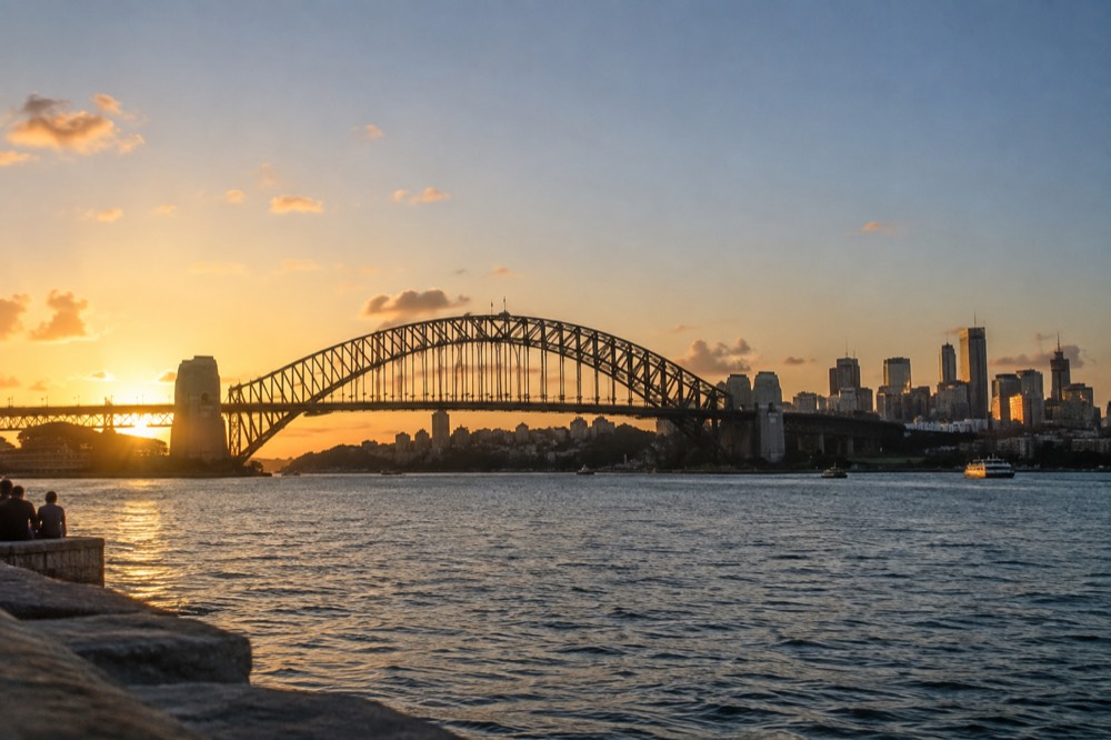 The Sydney Harbour Bridge arch seen from the harbour at dusk with the city skyline behind