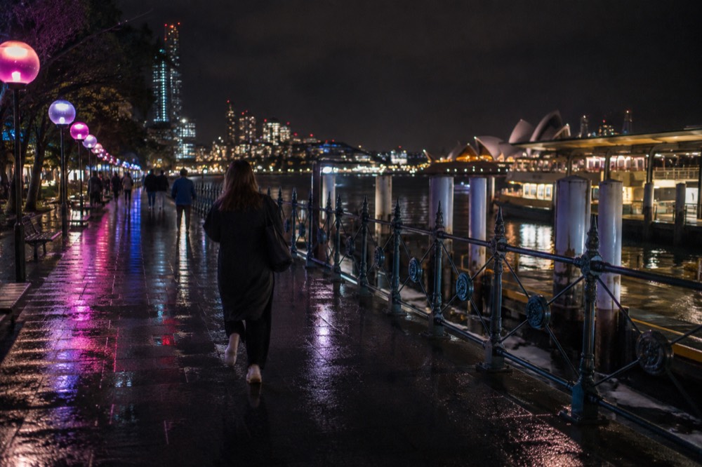 Festival lights reflecting on wet pavement along a harbour promenade at night