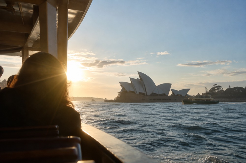 Ferry on blue harbour water with the white Opera House sails rising behind it