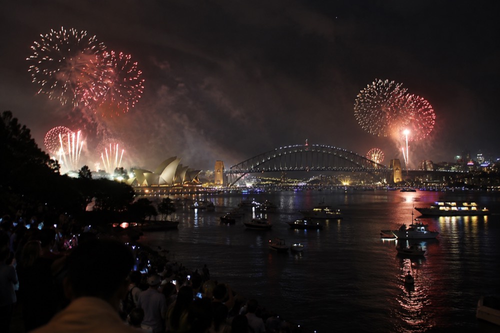 Sydney Harbour at night with fireworks bursting above the Opera House and Harbour Bridge