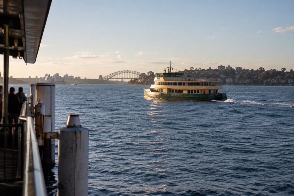A Sydney ferry crossing open harbour water toward a headland township