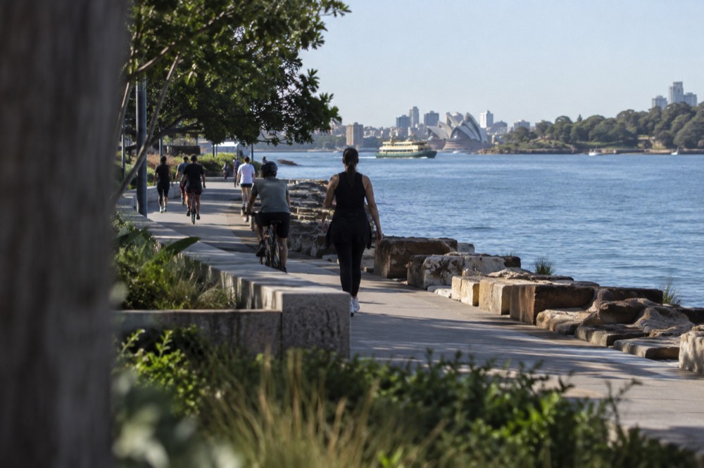Wide foreshore promenade with cyclists and walkers beside a calm harbour