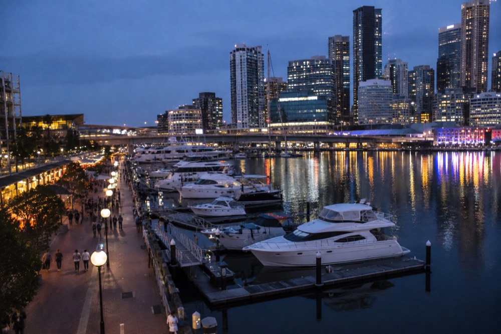 Waterfront promenade of Darling Harbour with high-rise buildings behind moored boats