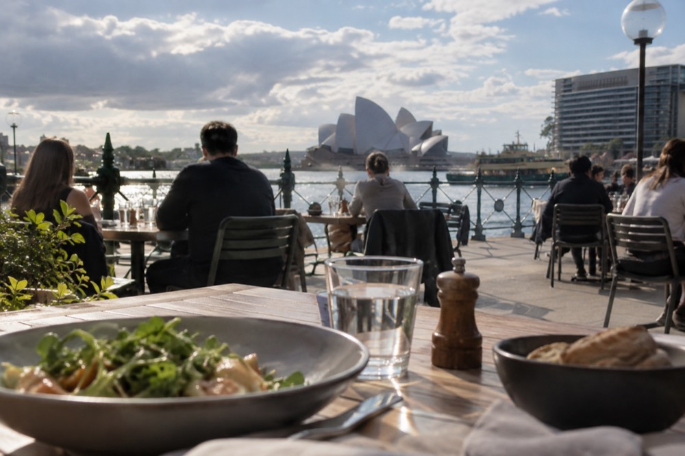 Diners at outdoor tables along the Circular Quay promenade facing the harbour