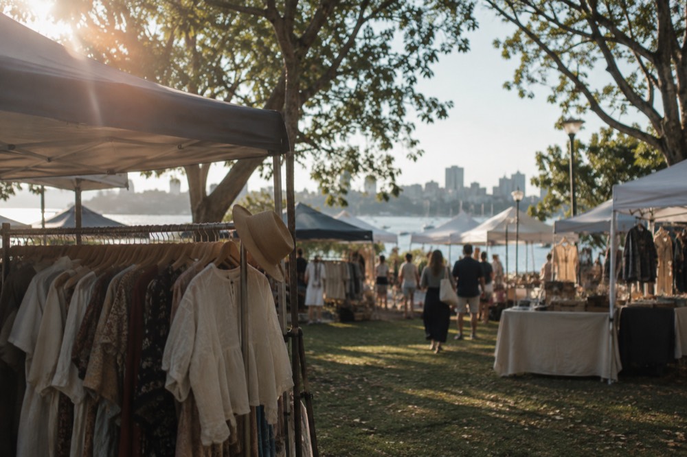 Market stalls with clothing racks and canvas tents set up among trees