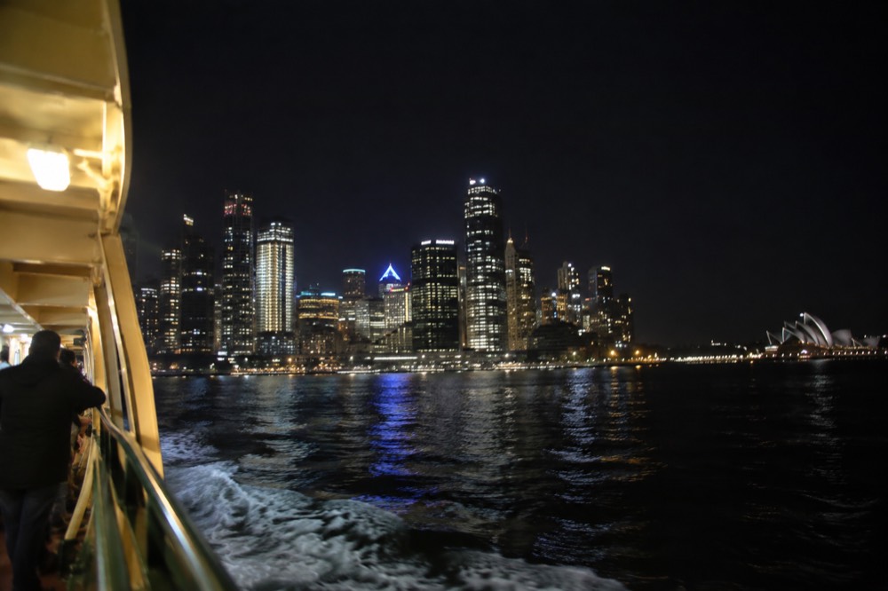 Sydney skyline and harbour lit up at night from a ferry on the water