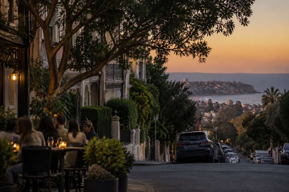 Cafe tables on a tree-lined street with terrace houses behind