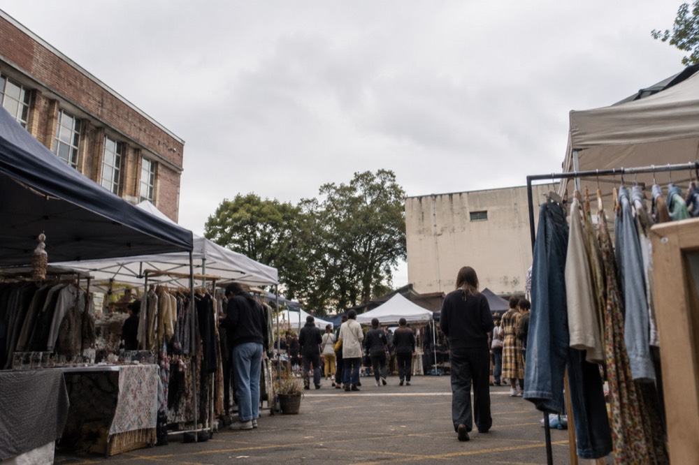 Market stalls with clothing racks and canvas awnings in a schoolyard