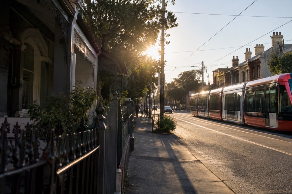 A light rail tram passing a row of terrace houses with corrugated iron fences