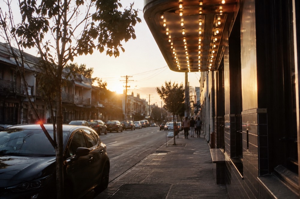 A small theatre facade lit by rows of bare bulbs above a narrow street at dusk