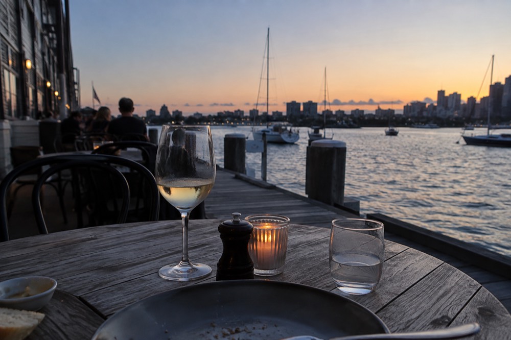 Outdoor cafe tables beside a wharf building with boats visible on the water