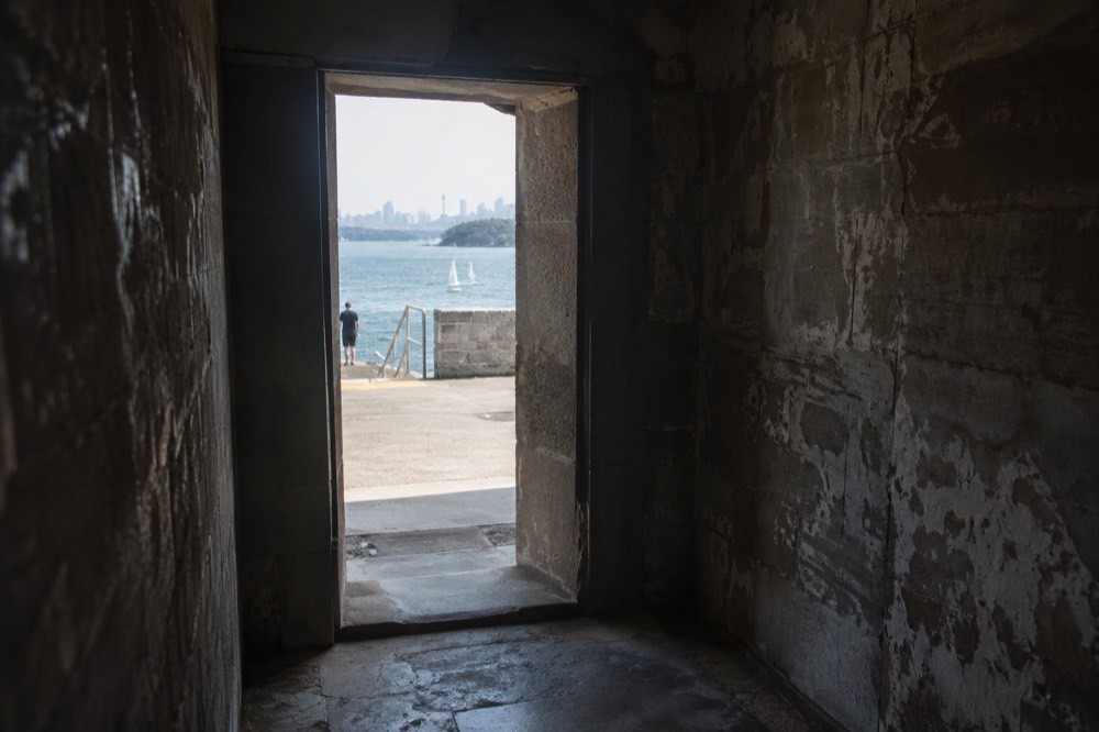 Dark interior of a stone solitary confinement cell with a small doorway opening to daylight
