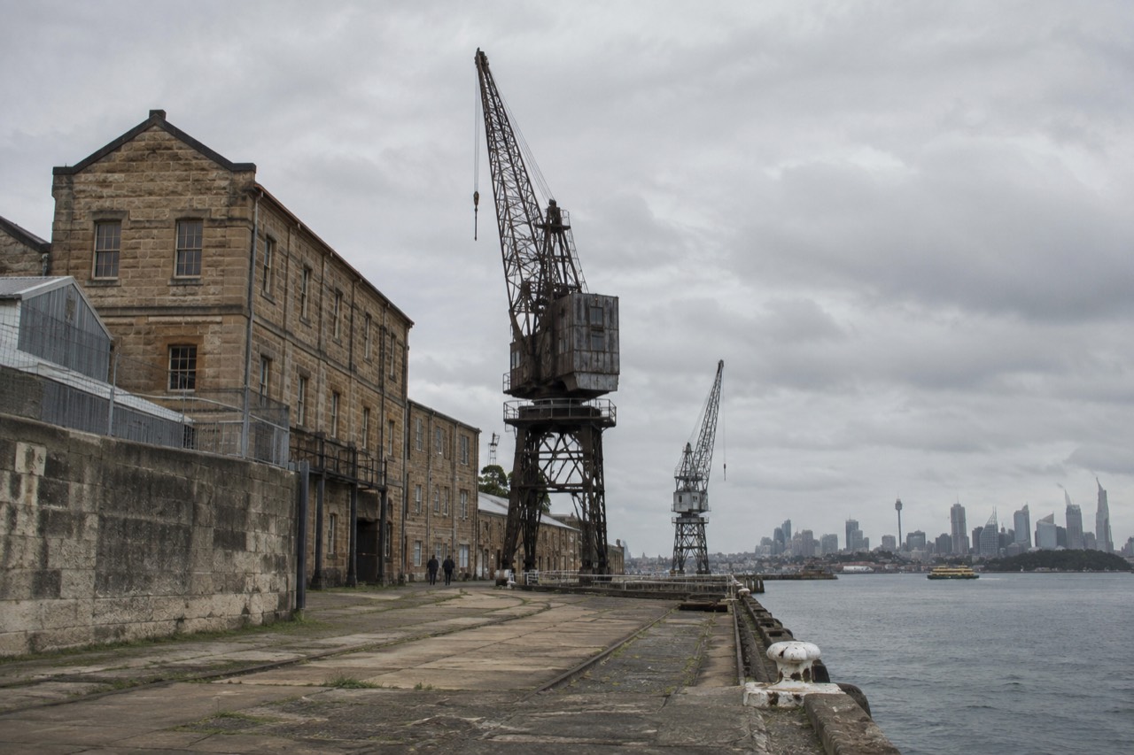 Sandstone convict-era buildings and old dockyard cranes on Cockatoo Island with Sydney Harbour in the background