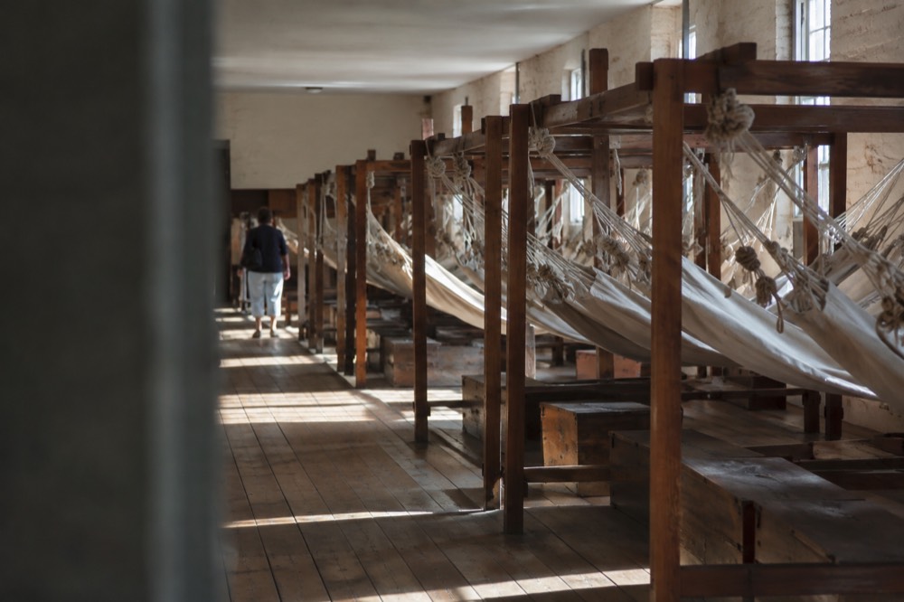 A long museum room with rows of replica fabric hammocks slung from wooden frames
