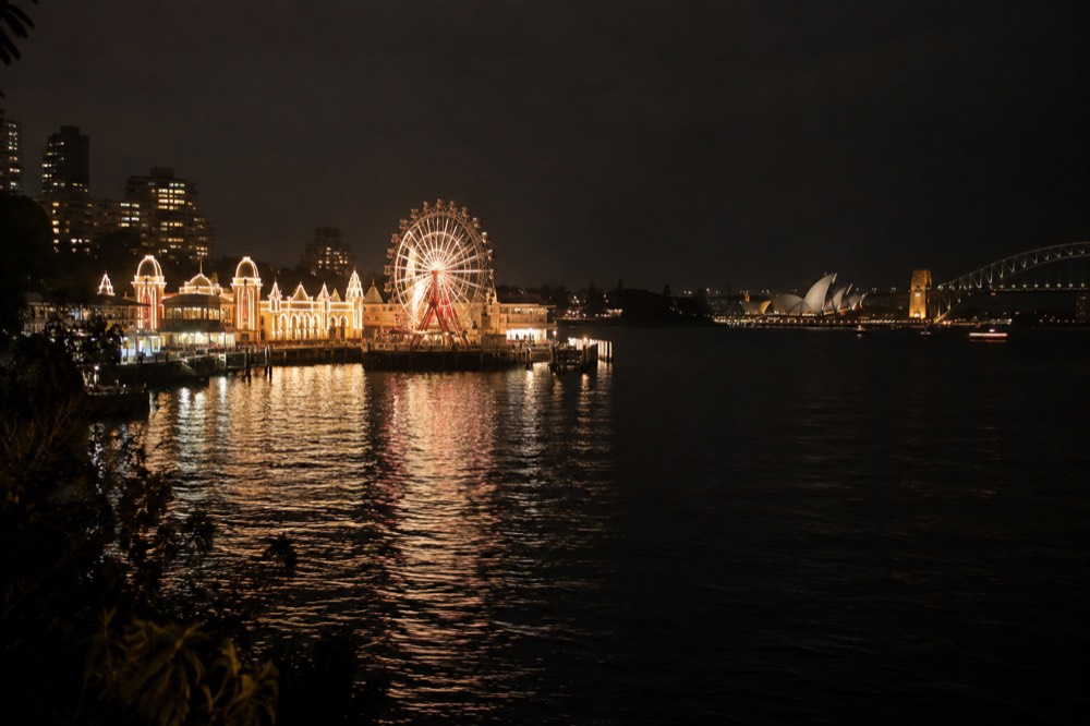 A lit Ferris wheel at night seen across dark harbour water