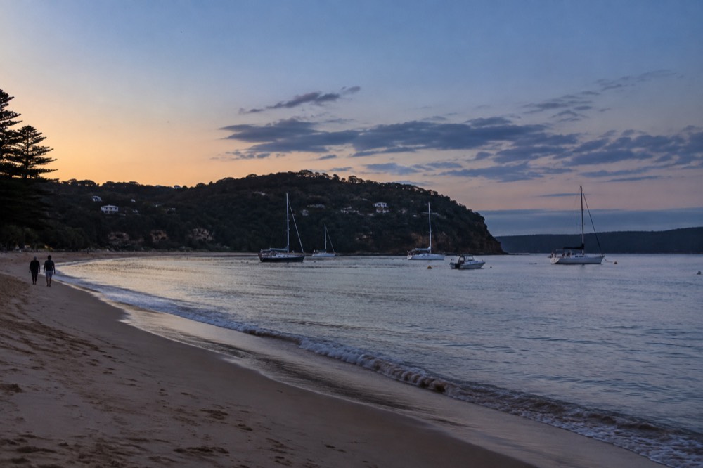 Calm sheltered water with moored sailing boats and a sandy shoreline