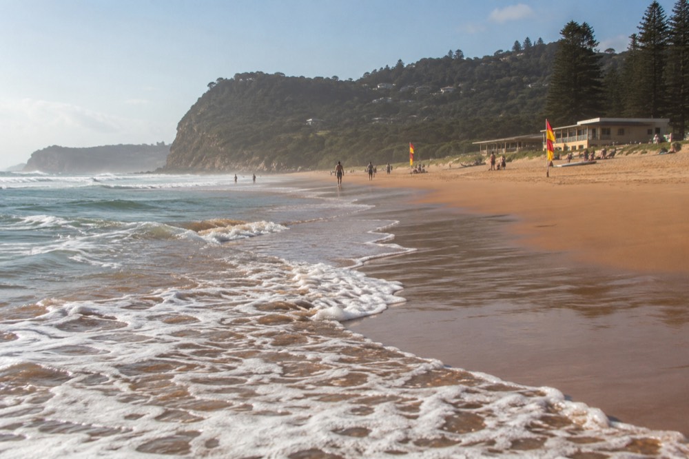 Red and yellow patrol flags on a wide beach with a surf club building behind