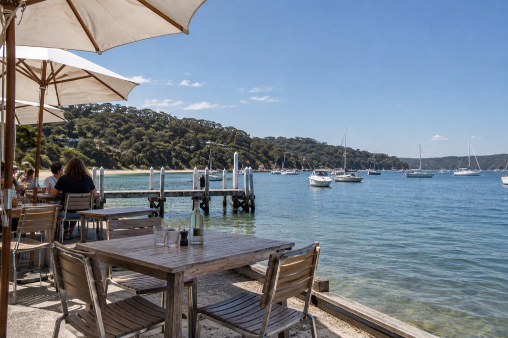 Waterfront cafe tables beside a jetty on calm water with boats