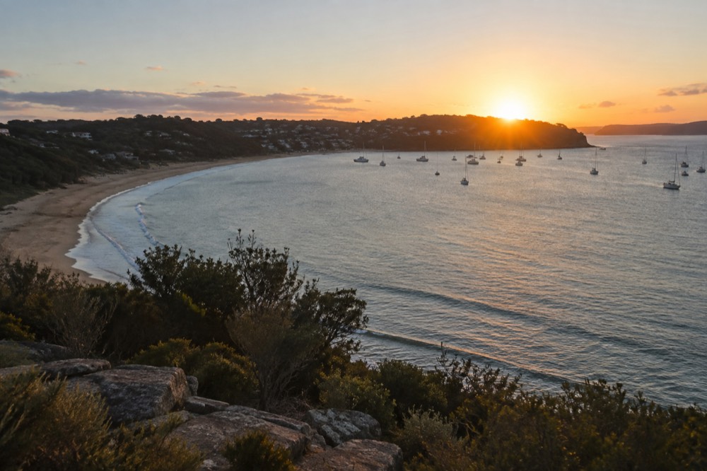 Sunset light over a headland and calm bay with boats at anchor