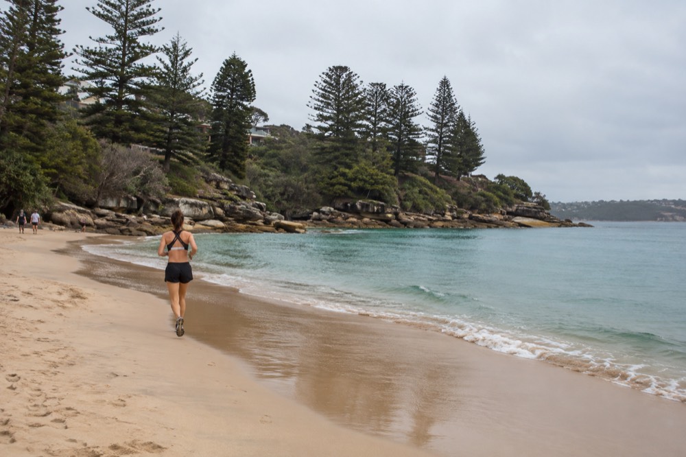 A sheltered sandy cove with calm turquoise water and a rocky headland with pine trees