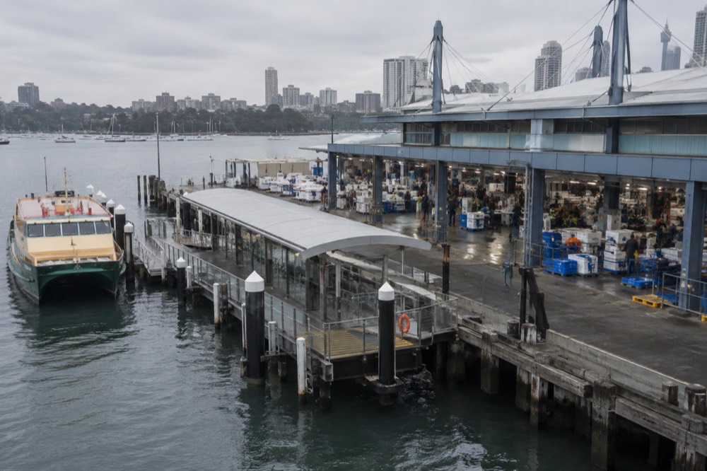 A ferry wharf on a calm city bay with a market building behind it