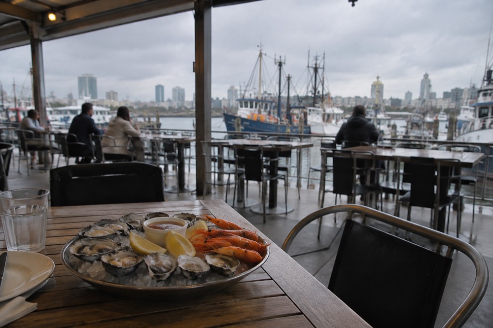 A covered market dining area with tables looking out over moored boats
