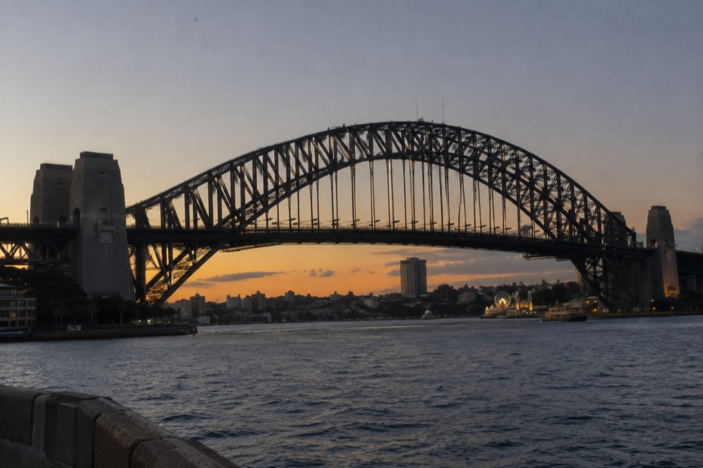 Climbers in grey suits walking along the outer arch of the bridge at twilight