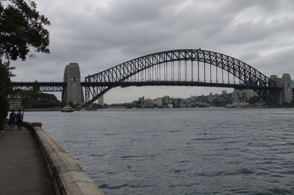 A train crossing the bridge seen from the Milsons Point foreshore with the arch behind