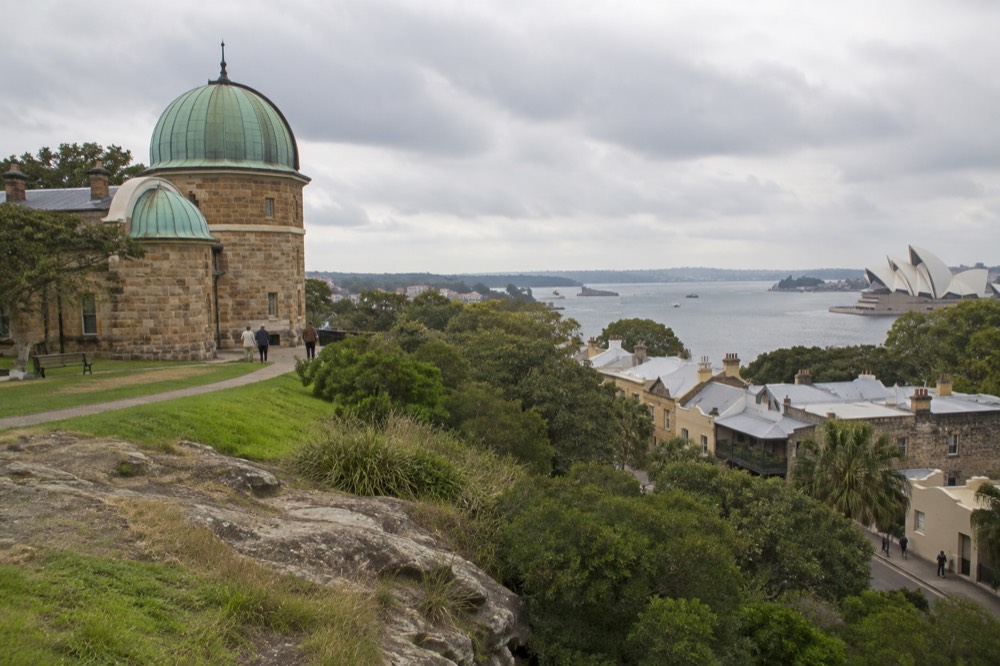 Historic sandstone laneways and terrace buildings below a green hill in an old harbour-side district