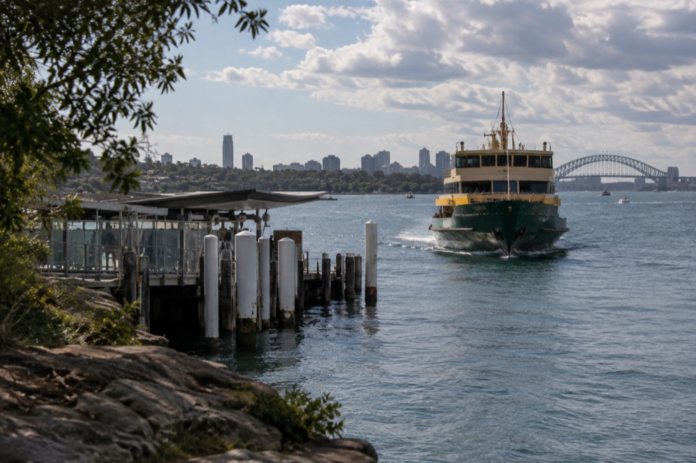 A green and yellow ferry approaching a wharf on a calm harbour
