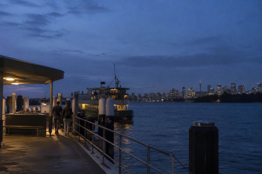 A ferry wharf at dusk with the city skyline lit across the water