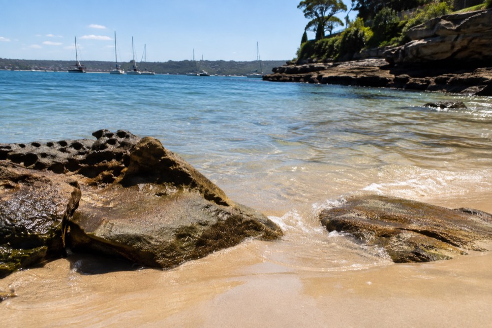 Calm harbour beach with clear shallow water and sandstone rocks at the waterline