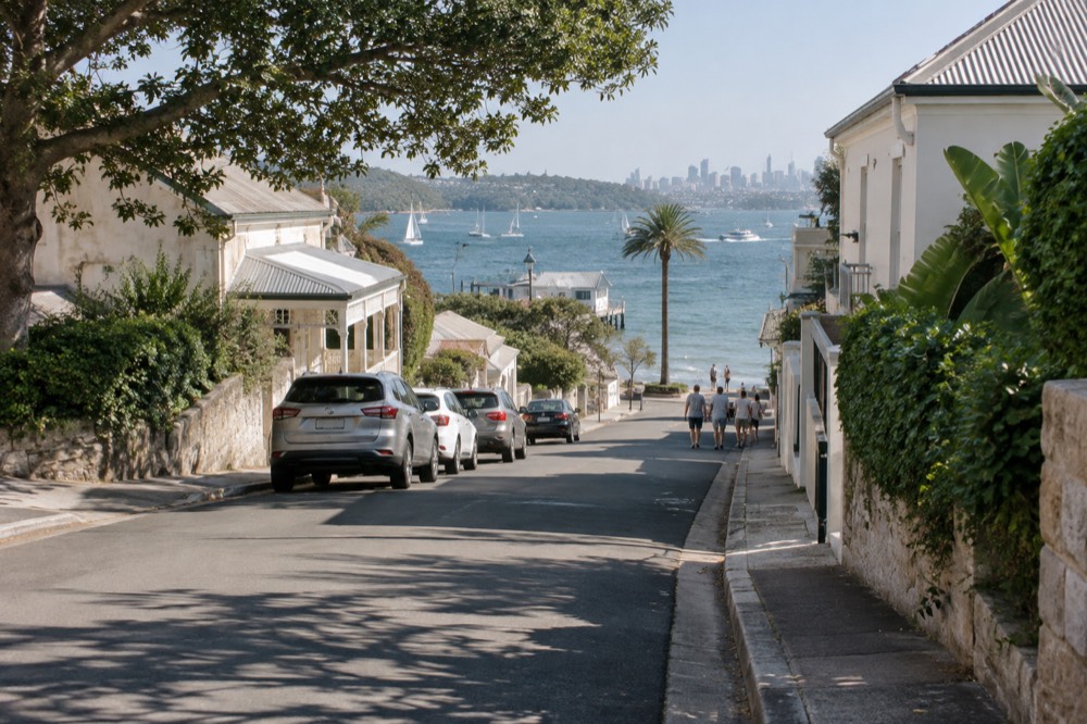 Village main street with low heritage buildings and a glimpse of harbour water at the end