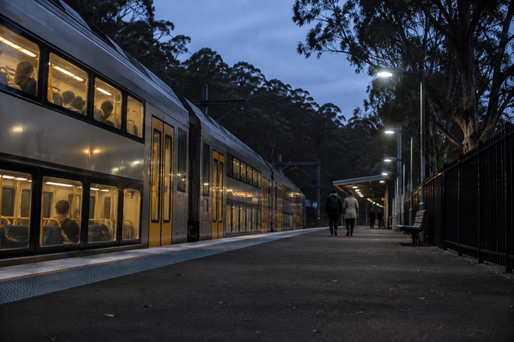 A double-deck train at a Blue Mountains station with eucalypt forest behind
