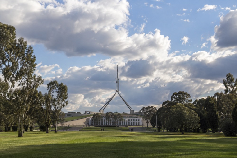 Modern parliament building with flag pole rising above lawns and eucalyptus trees