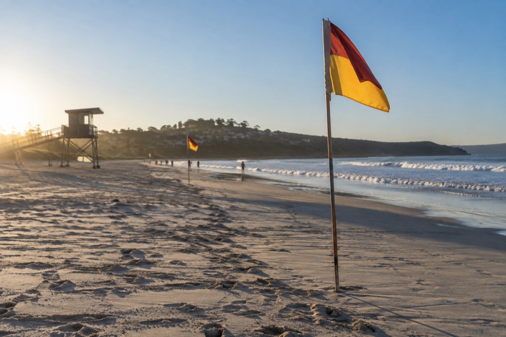 Red and yellow patrol flags on a wide sandy beach with a lifeguard tower