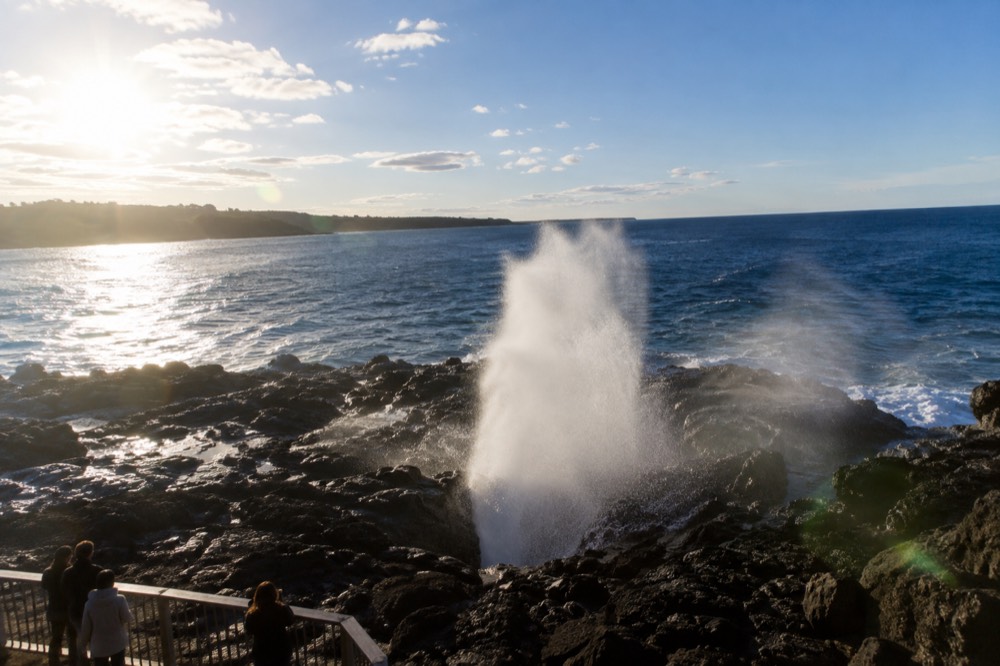 Ocean spray rising from a coastal blowhole against a blue sky