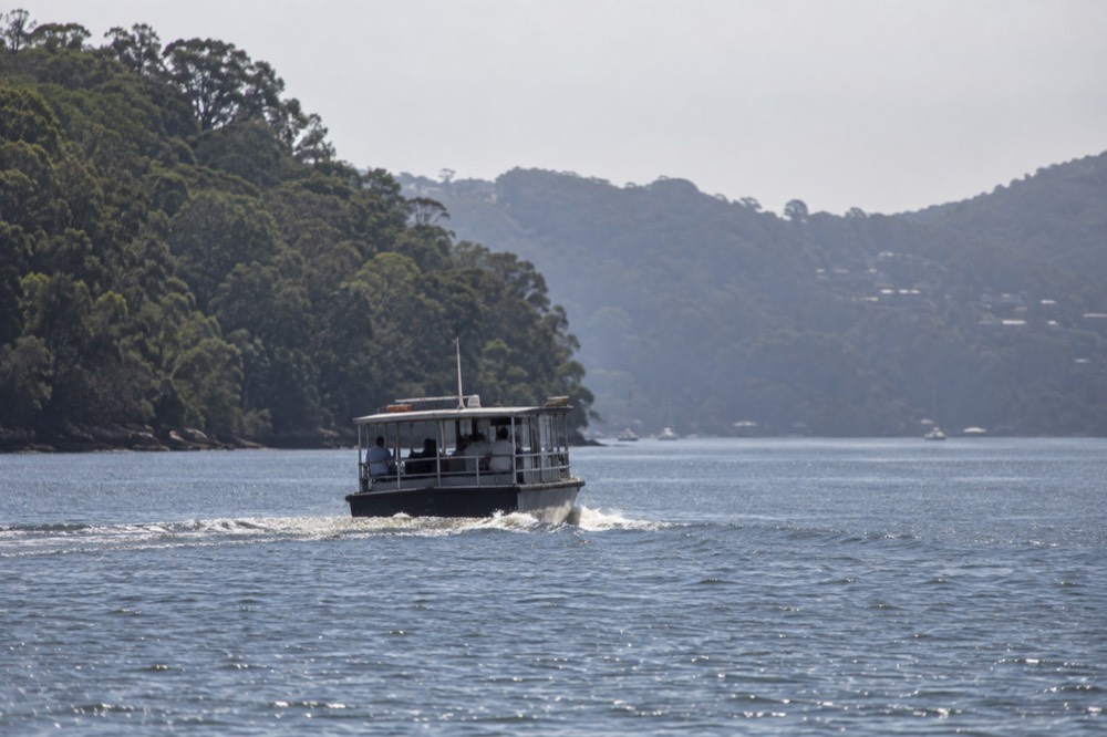 A small passenger ferry crossing a wide river towards a forested bank