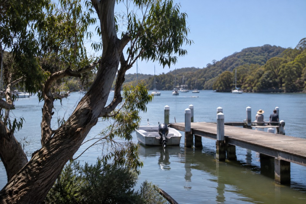 Still river water in a sheltered cove with a wooden jetty and forested slopes