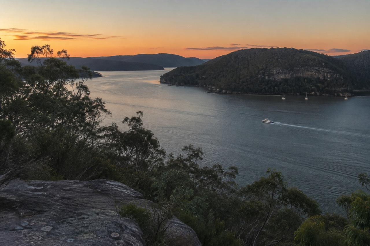 Wide view of a calm river estuary with sandstone headlands and dense bushland on both shores