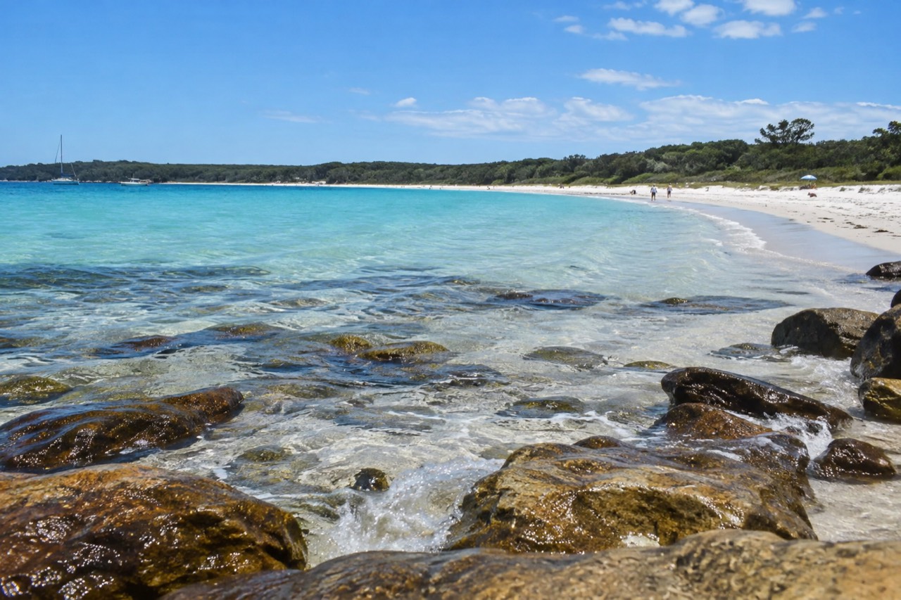 Turquoise water curving along a white sand beach backed by low green bushland