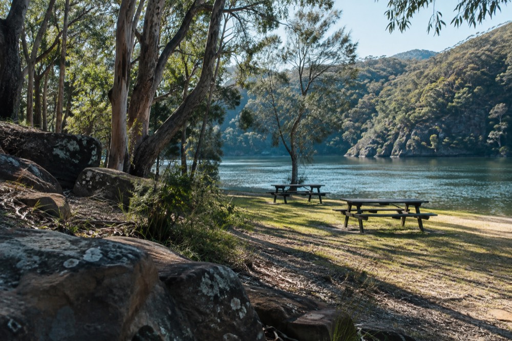 Picnic tables on a lawn beside calm creek water at Bobbin Head
