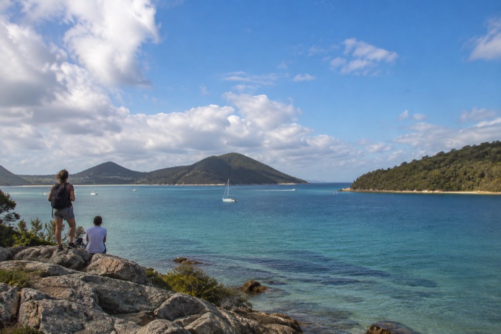 Calm turquoise bay water between green headlands under scattered clouds