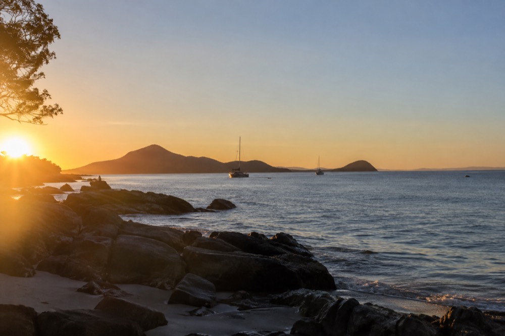 A calm bay at golden hour with headlands silhouetted against a clear sky