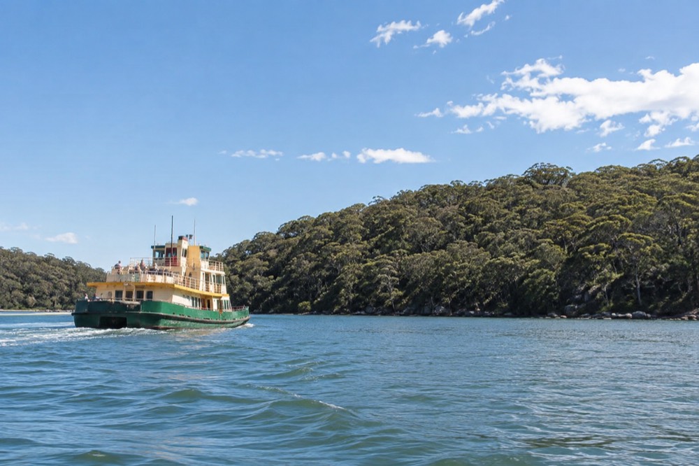 A ferry crossing a calm estuary toward a forested shoreline