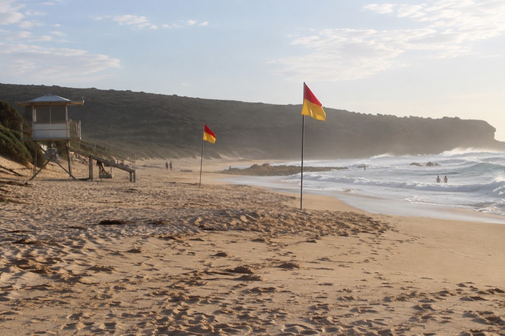 Red and yellow patrol flags on a sandy beach with a lifeguard tower behind