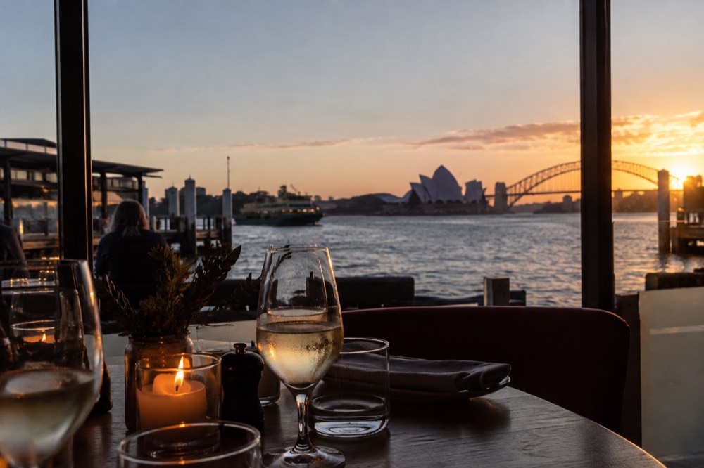 A candlelit restaurant table beside a window with a view of Sydney Harbour at dusk